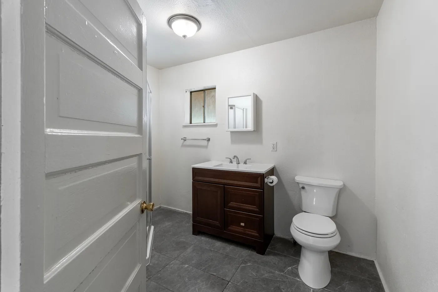 Renovated bathroom with a dark wood vanity, white walls and grey tile floor.