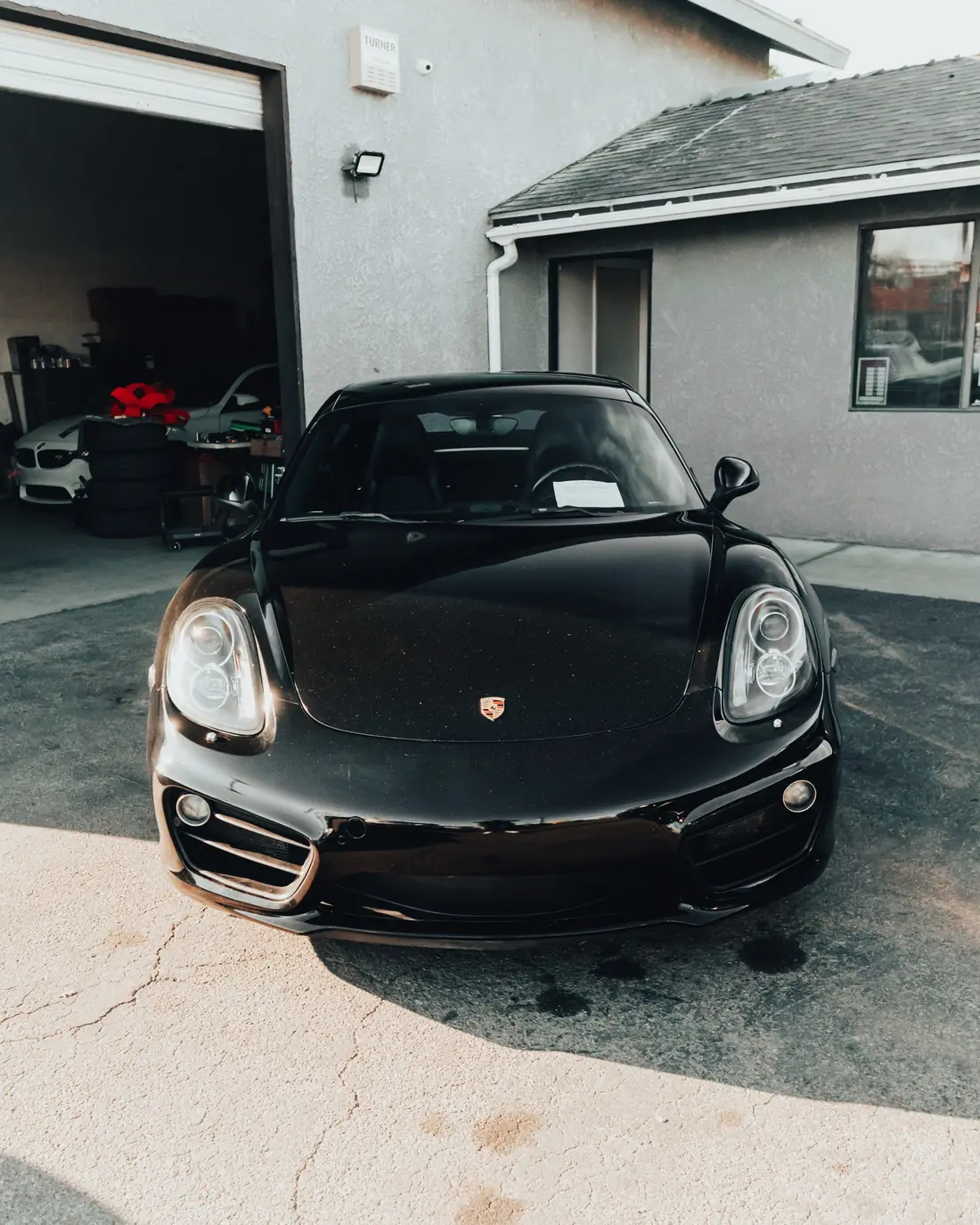 Black Porsche Cayman parked nose out on the apron in front of a shop unit.