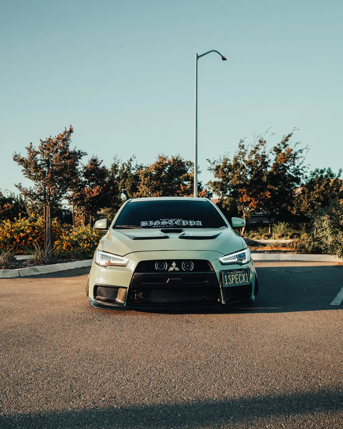 Modified Mitsubishi Lancer Evolution in sage green, shot head on at golden hour.