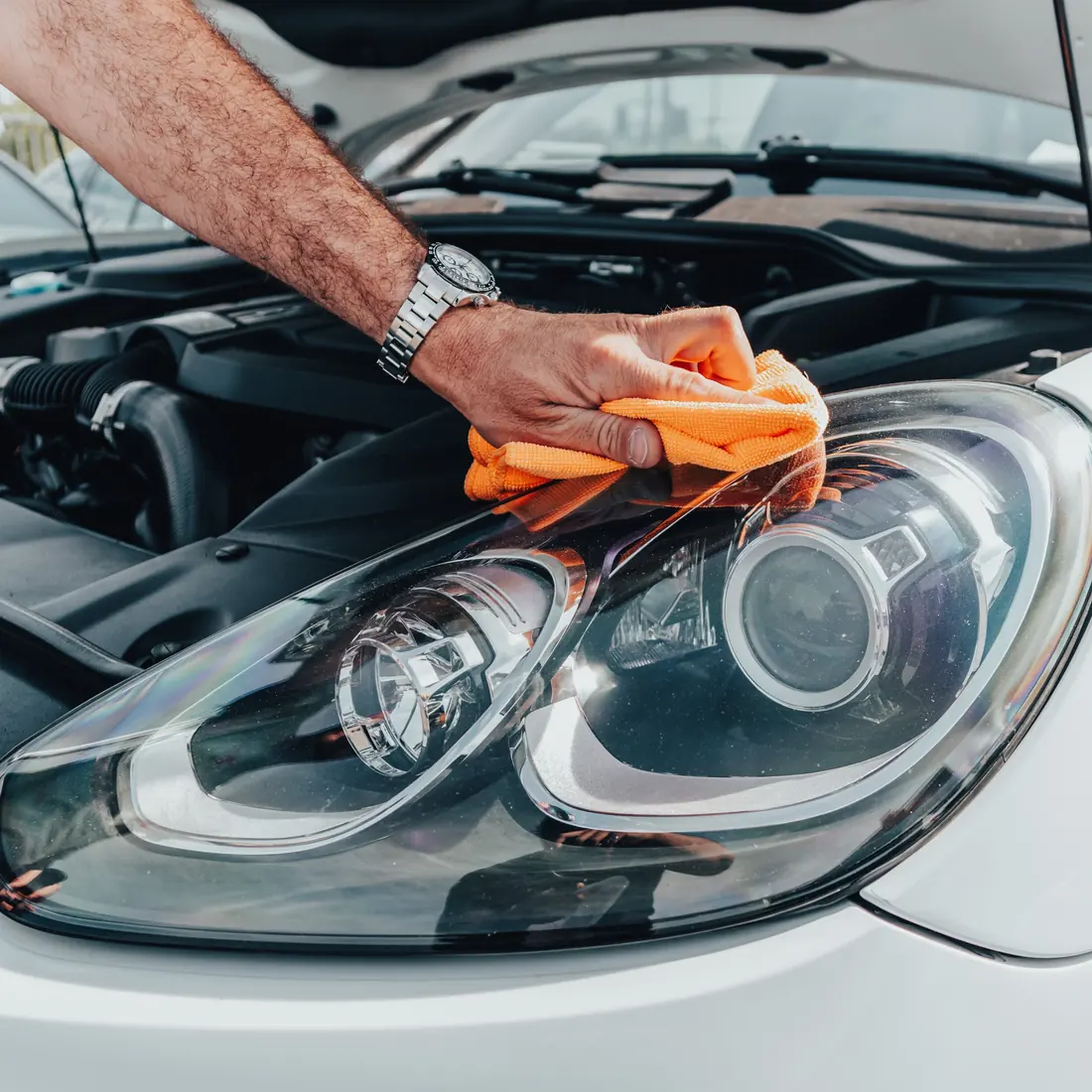 Close up of a detailer wiping a headlight with an orange microfiber cloth.